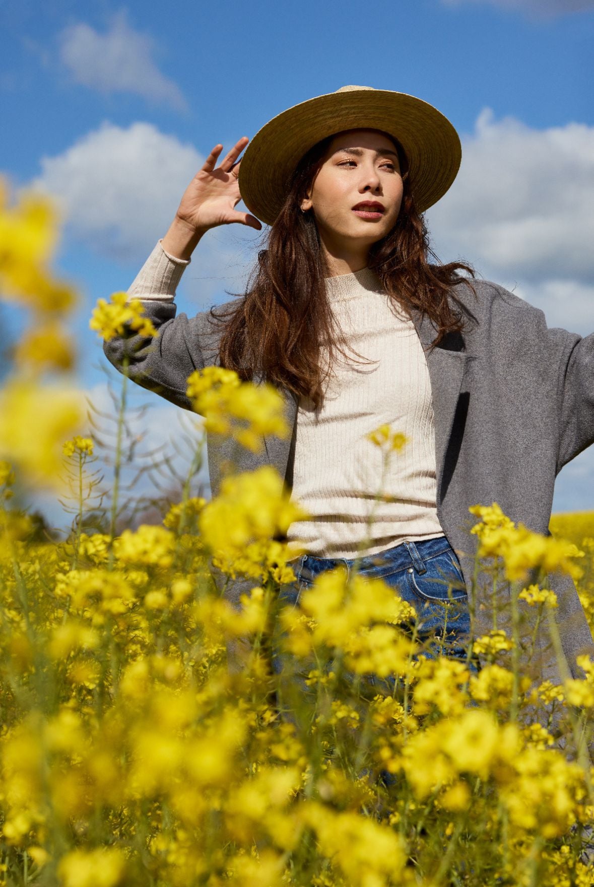 femme en chapeau et manteau se tenant dans un champ de fleurs jaunes.