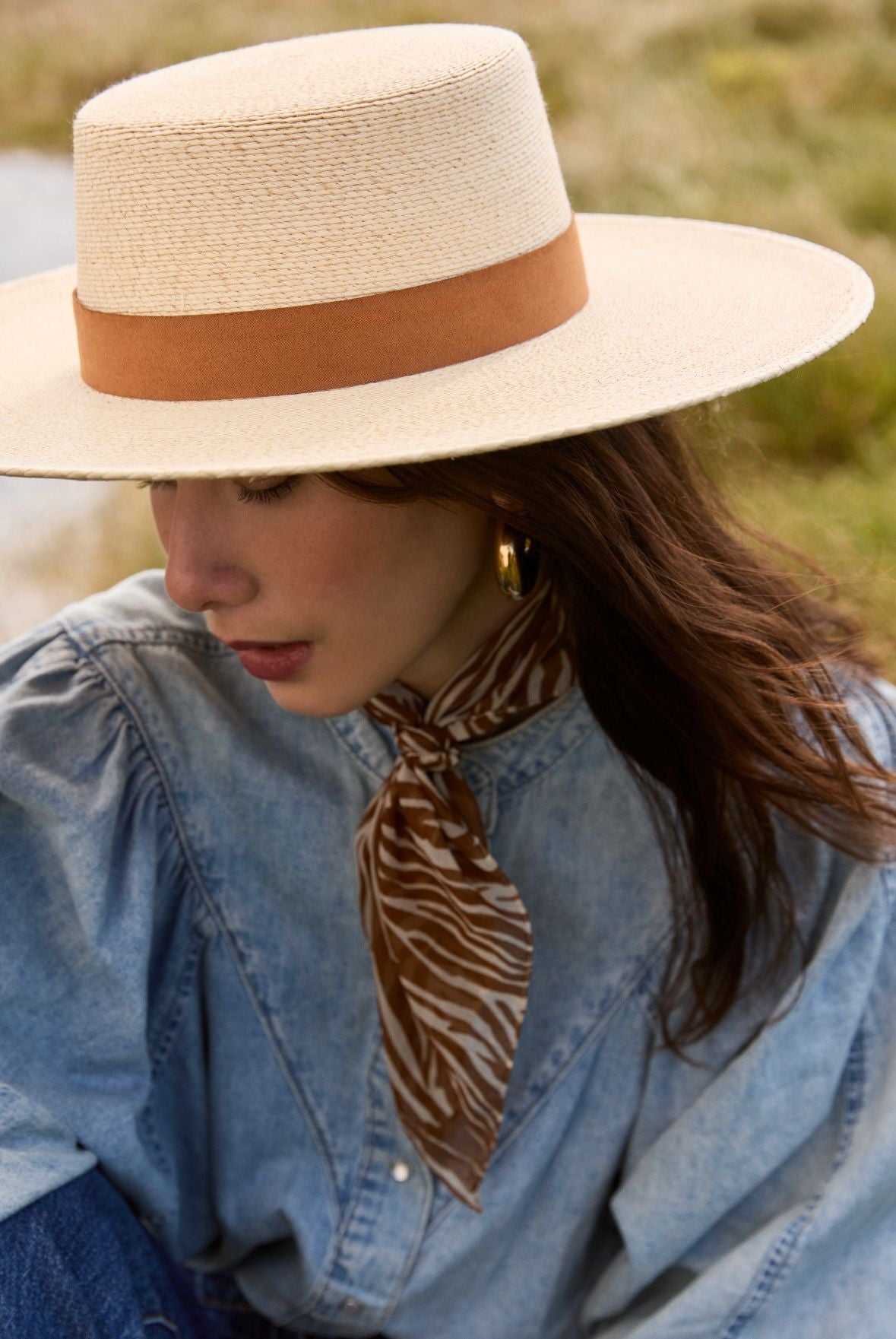 Une femme avec un chapeau de paille et un jean's assise dans l'herbe.