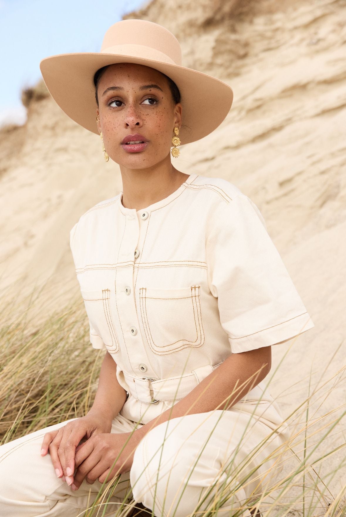 Femme portant une combinaison blanche et un chapeau sur la plage.