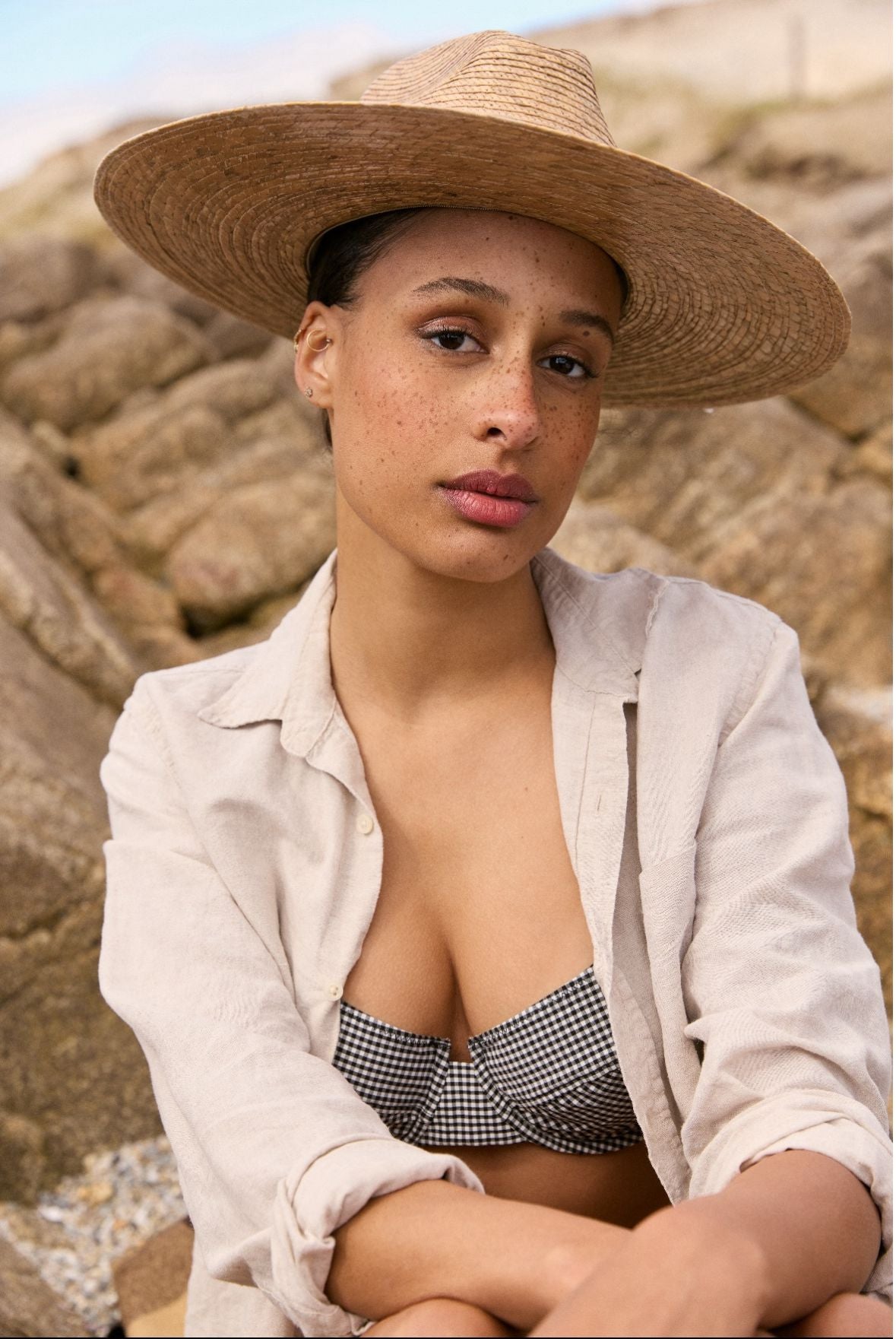 Femme en maillot de bain et chapeau de paille, assise sur des rochers.