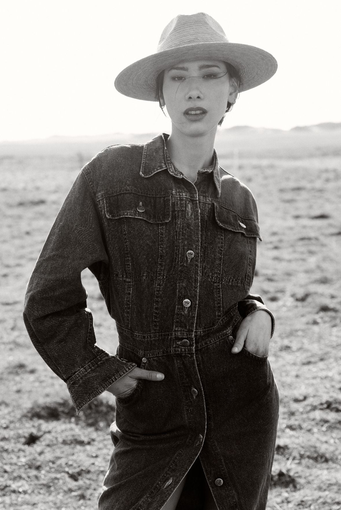 Femme vêtue d'une combinaison en jean et d'un chapeau, dans le désert.