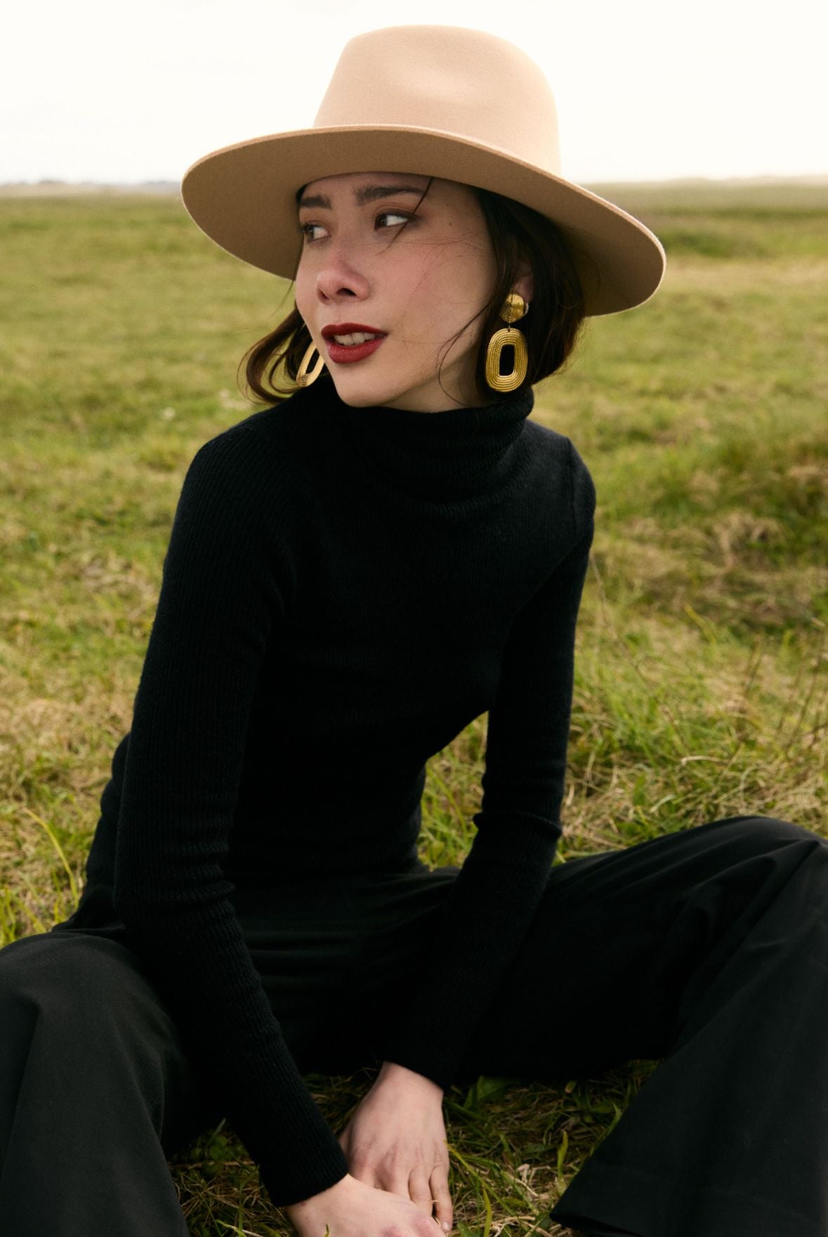 Une femme avec un chapeau assise dans un champ ensoleillé.