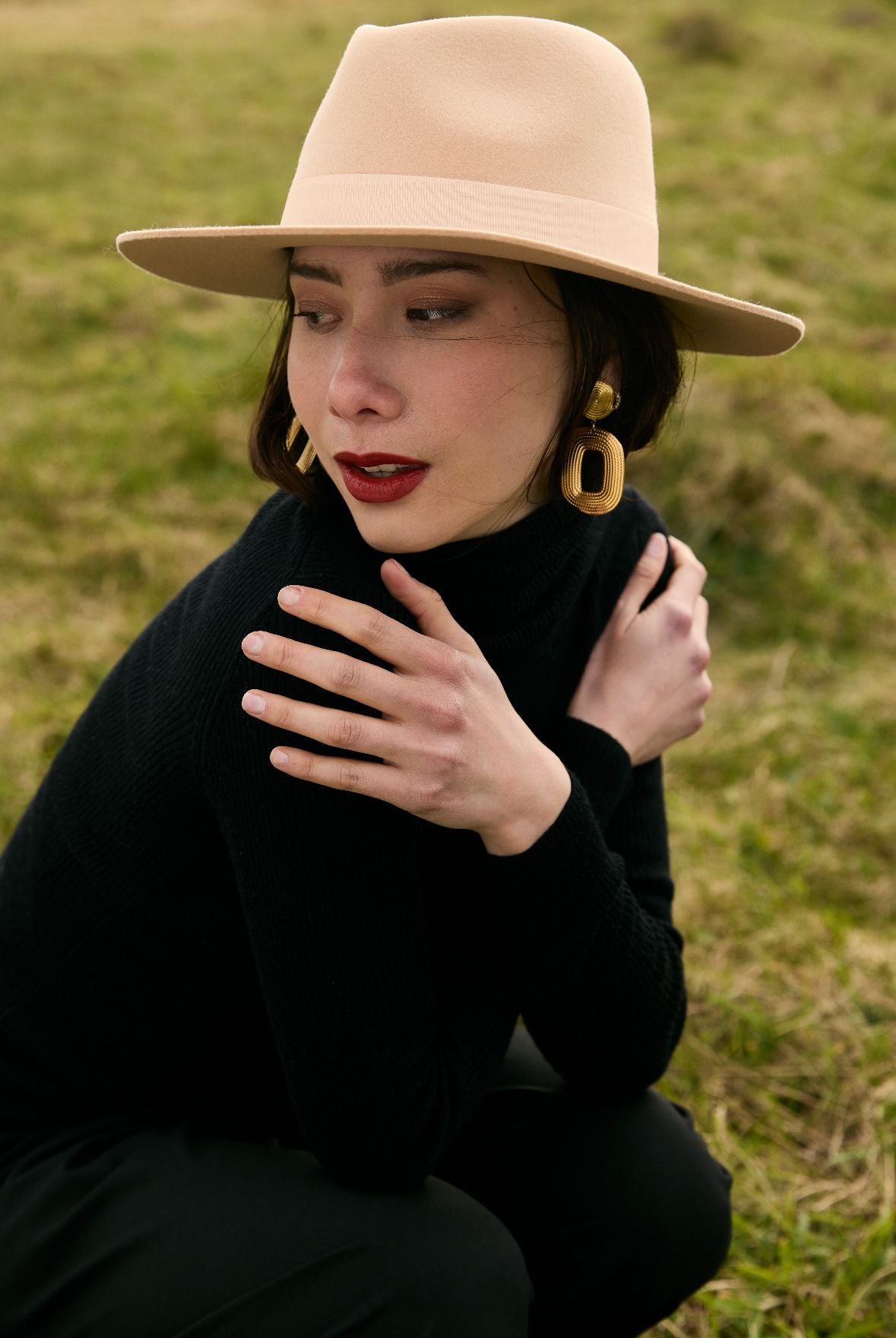Une femme avec un chapeau assise dans un champ ensoleillé.