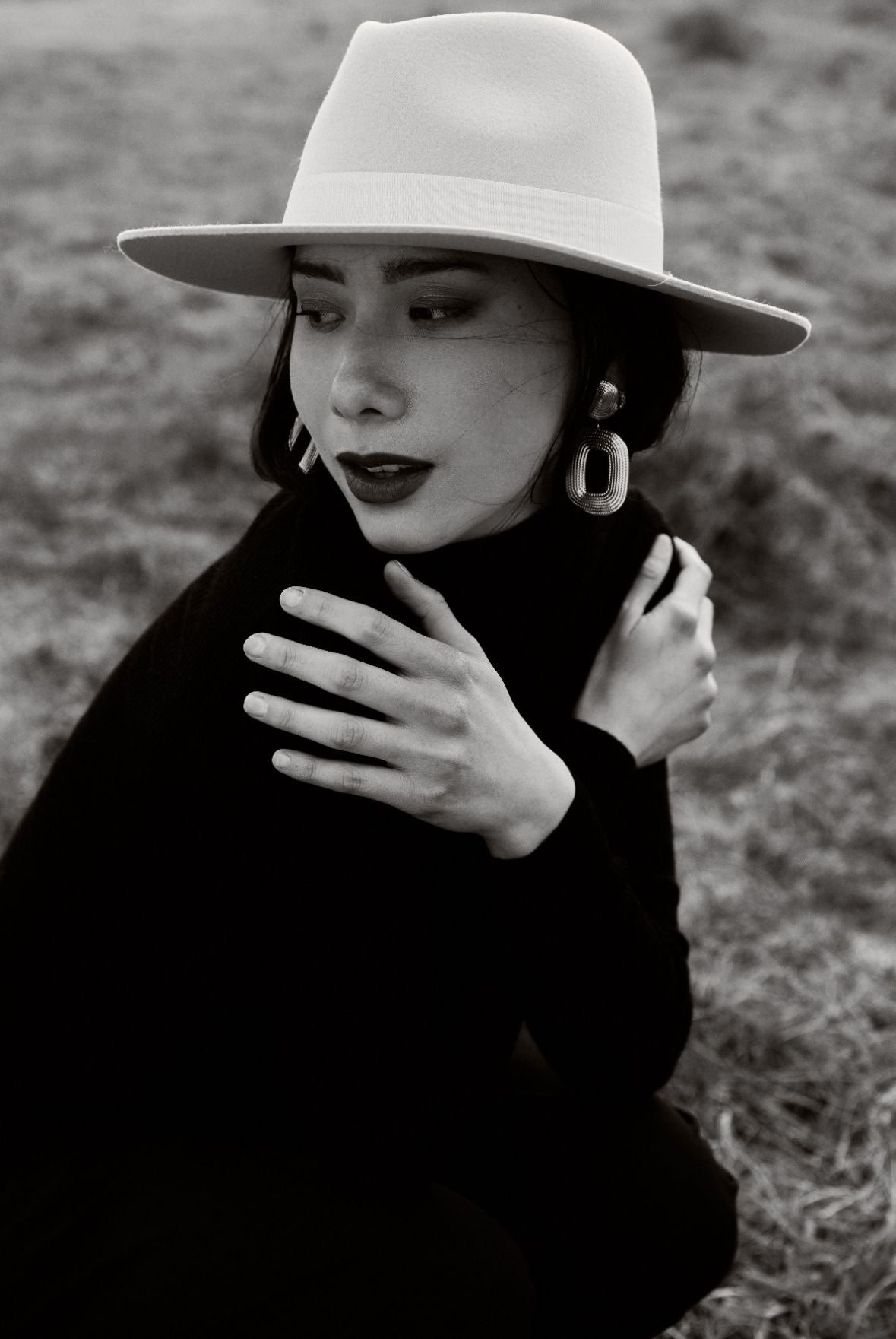 Une femme avec un chapeau assise dans un champ ensoleillé. noir et blanc 