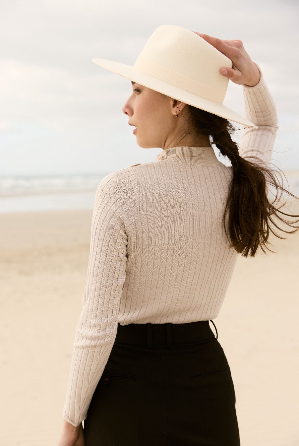 Femme portant un chapeau en feutre blanc et un pull sur la plage
