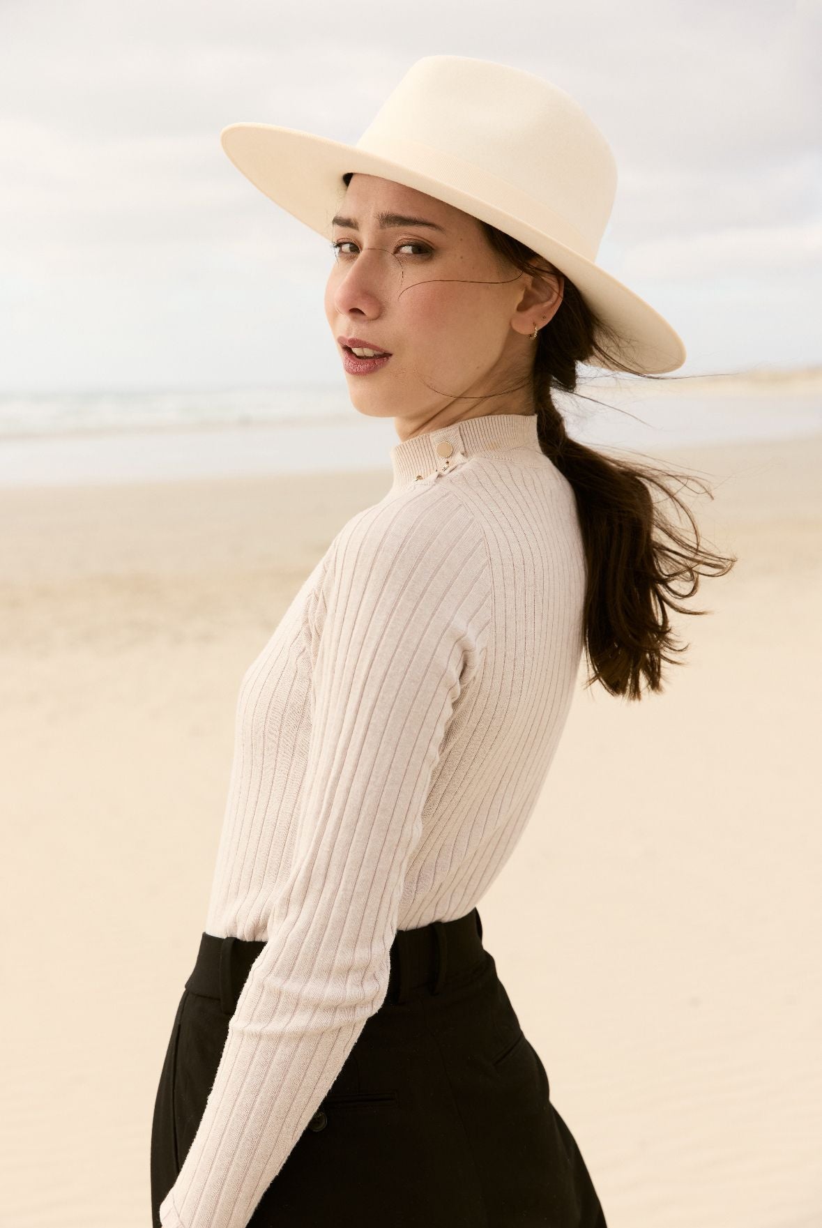 Femme portant un chapeau en feutre blanc  et un pull sur la plage
