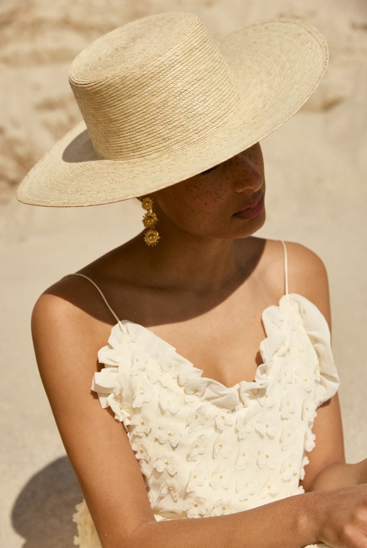 Femme en robe blanche et chapeau de paille assise sur la plage.