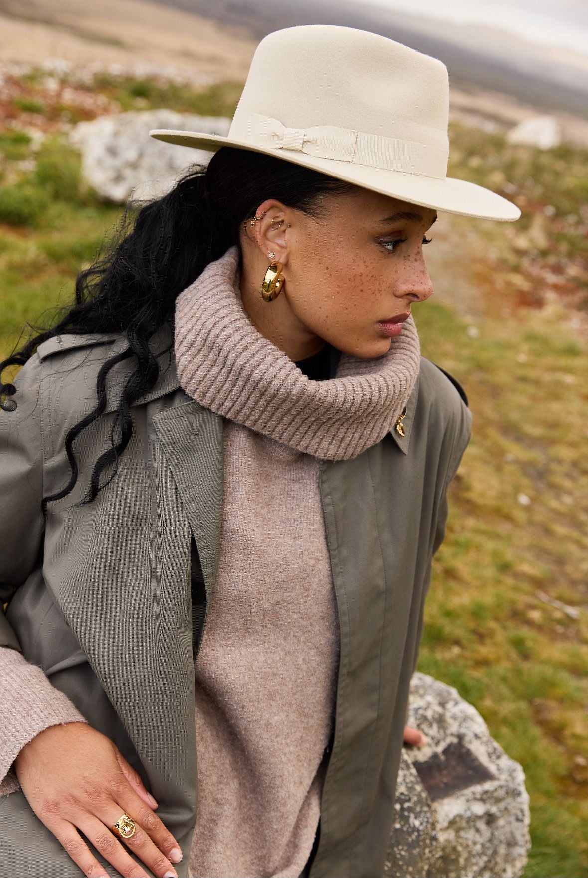 Une femme portant un chapeau en feutre de laine fabriqué en france et un manteau assise sur un rocher