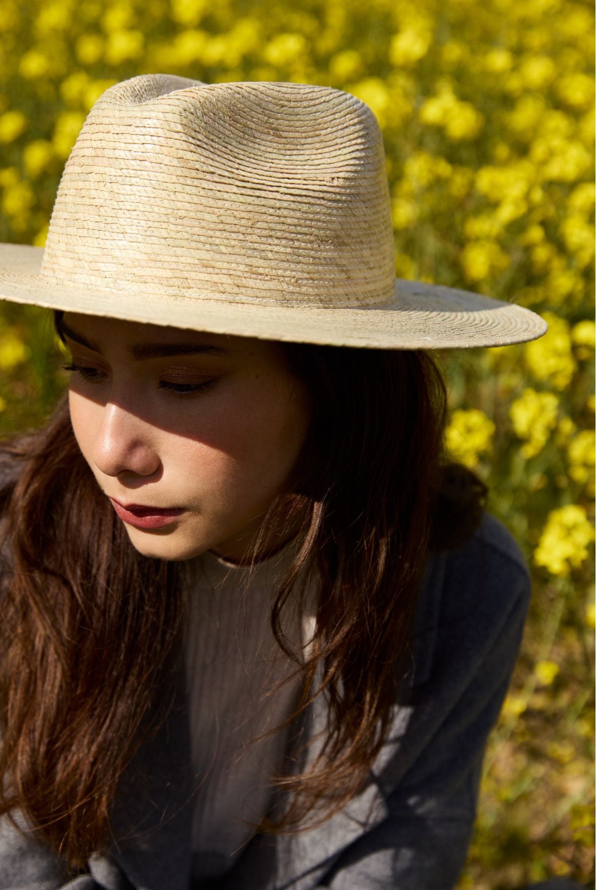 femme en chapeau et manteau se tenant dans un champ de colza
