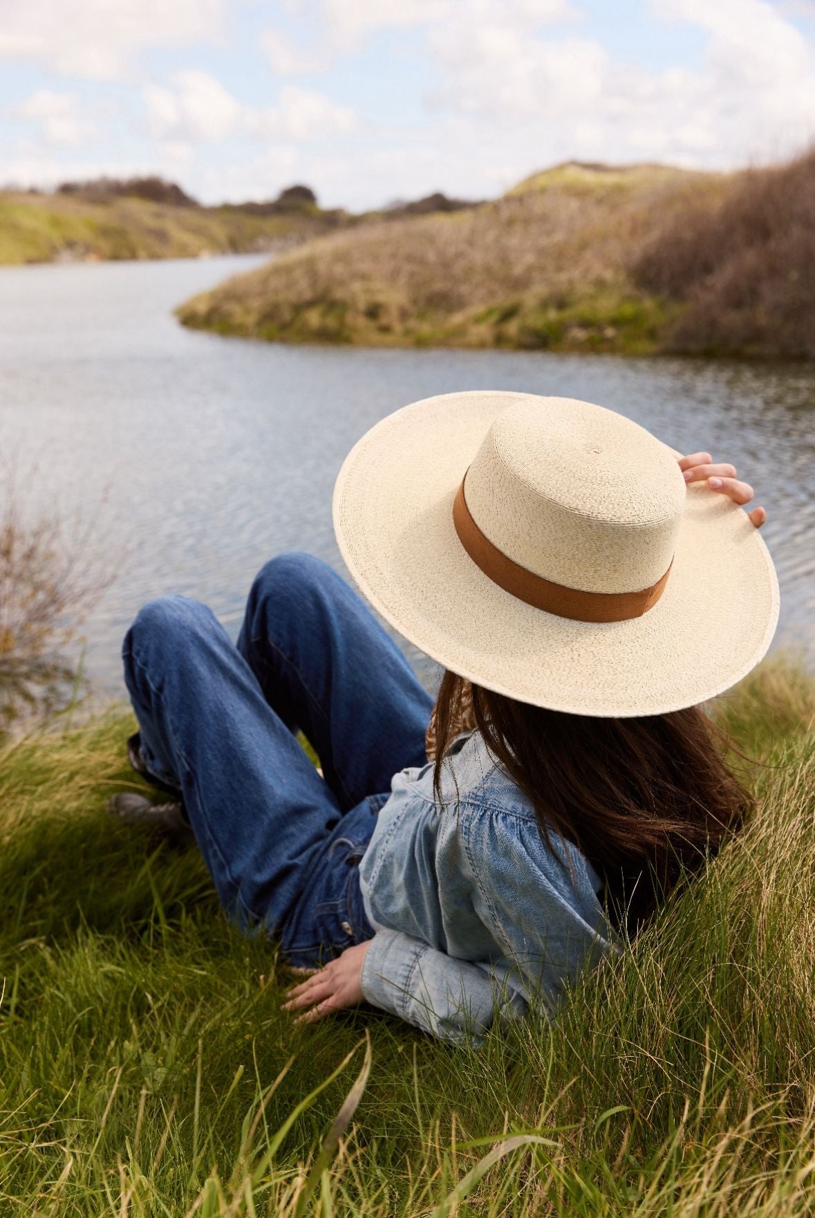 Une femme avec un chapeau de paille et un jean's assise dans l'herbe.