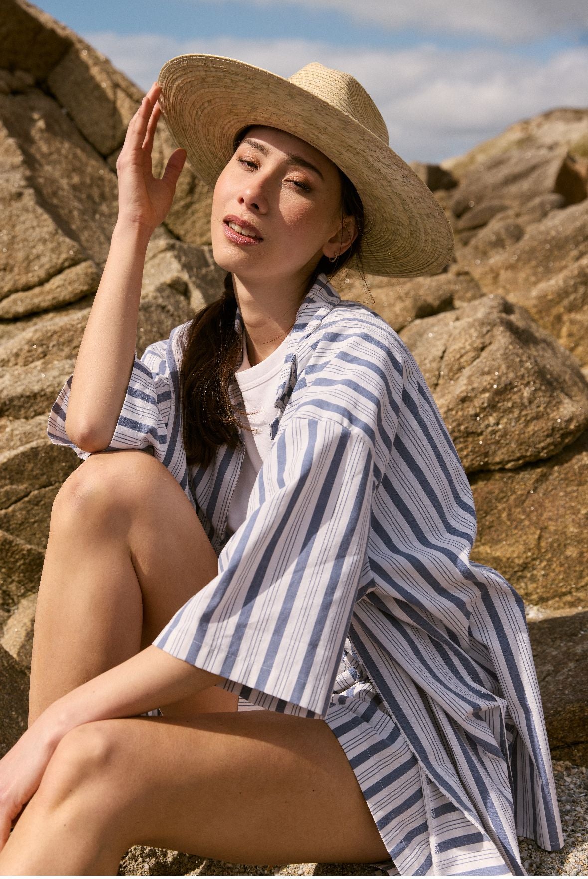 Une femme portant un chapeau de paille et une chemise assise sur des rochers.