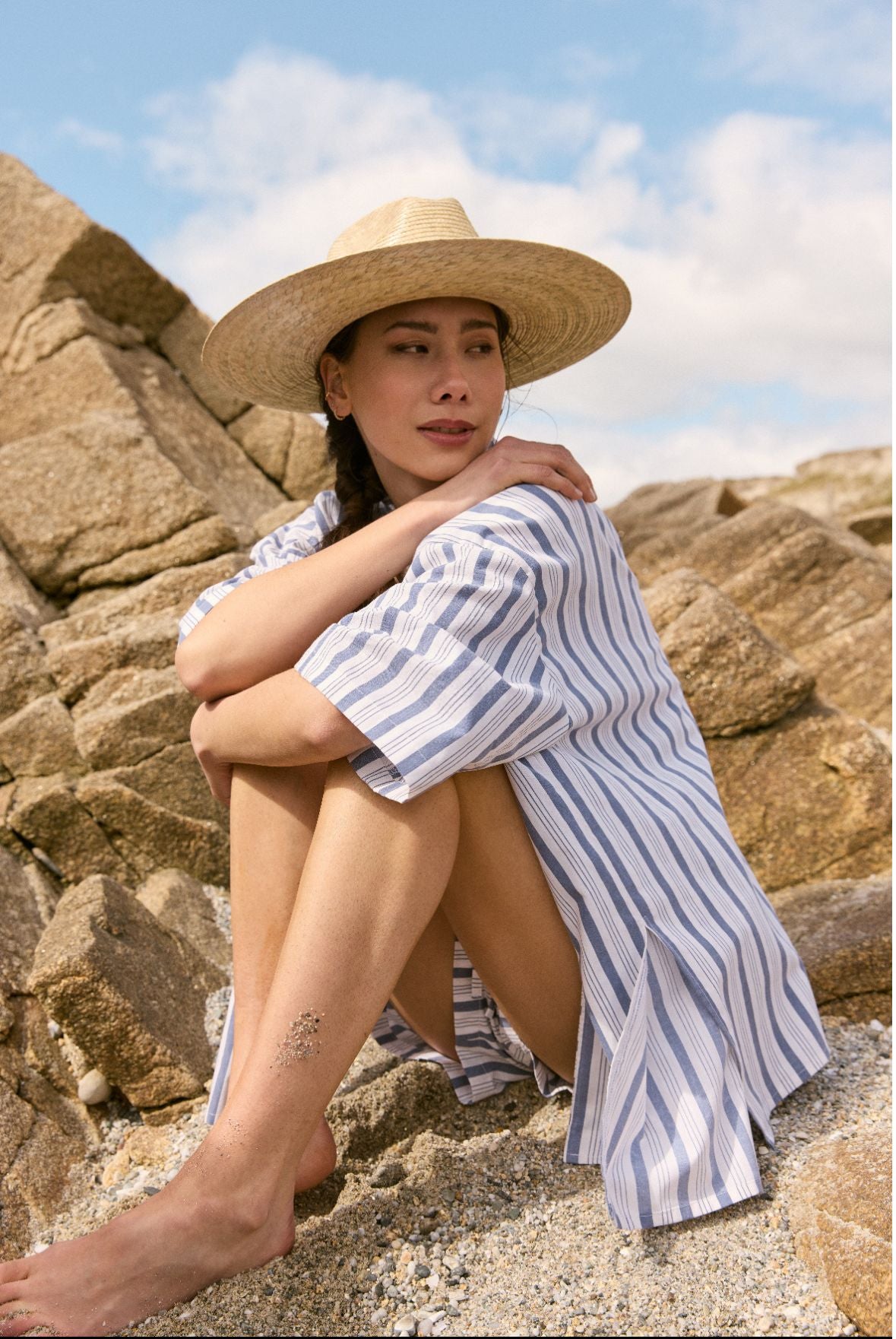 Une femme portant un chapeau de paille et une chemise assise dans le sable