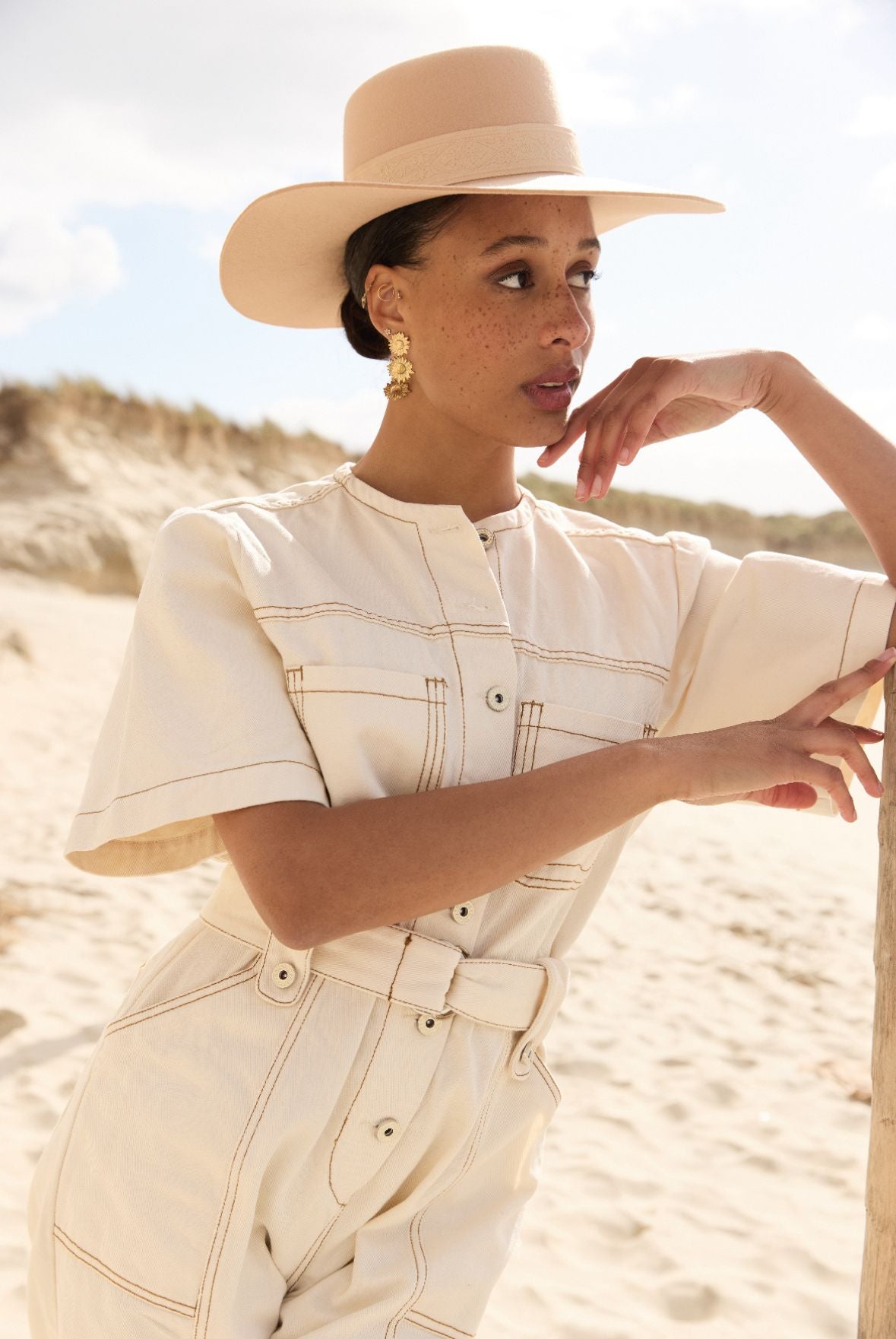 Femme portant une combinaison blanche et un chapeau sur la plage.