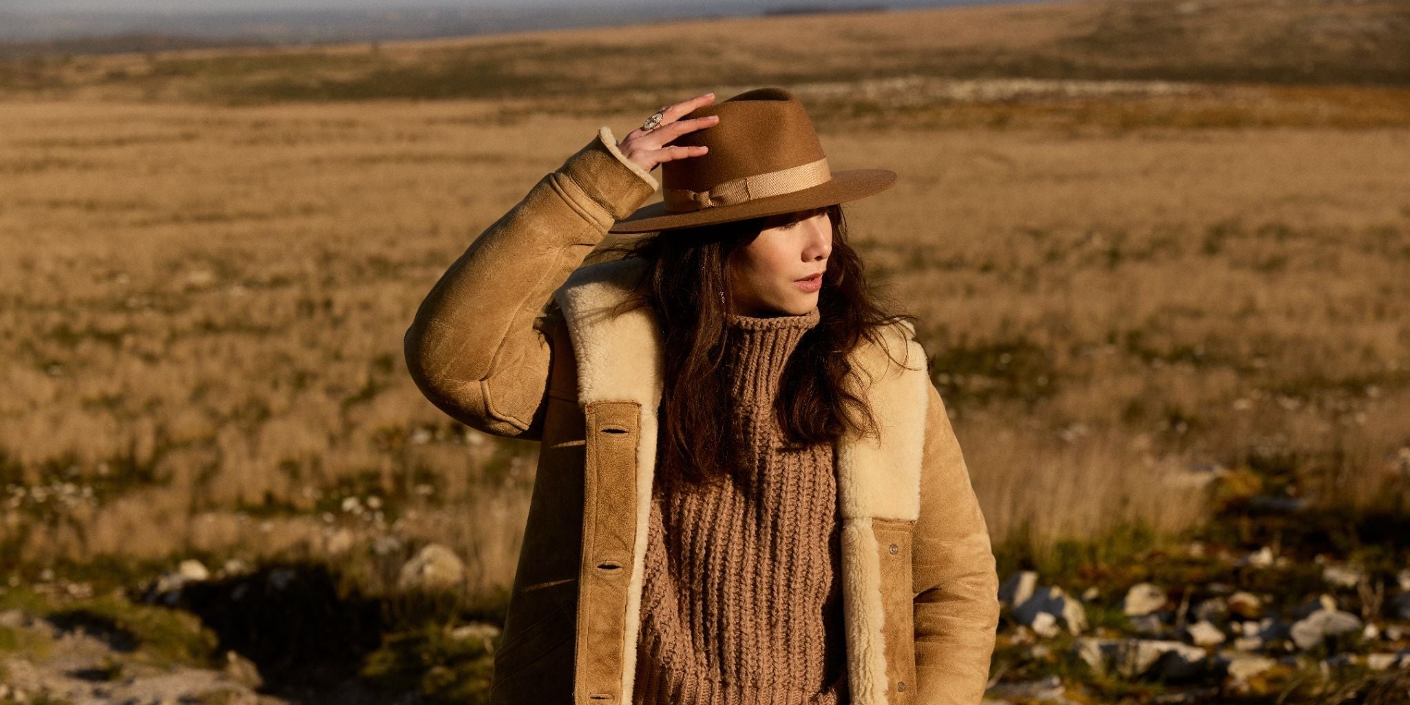 Une femme en manteau et chapeau marron debout dans un champ.