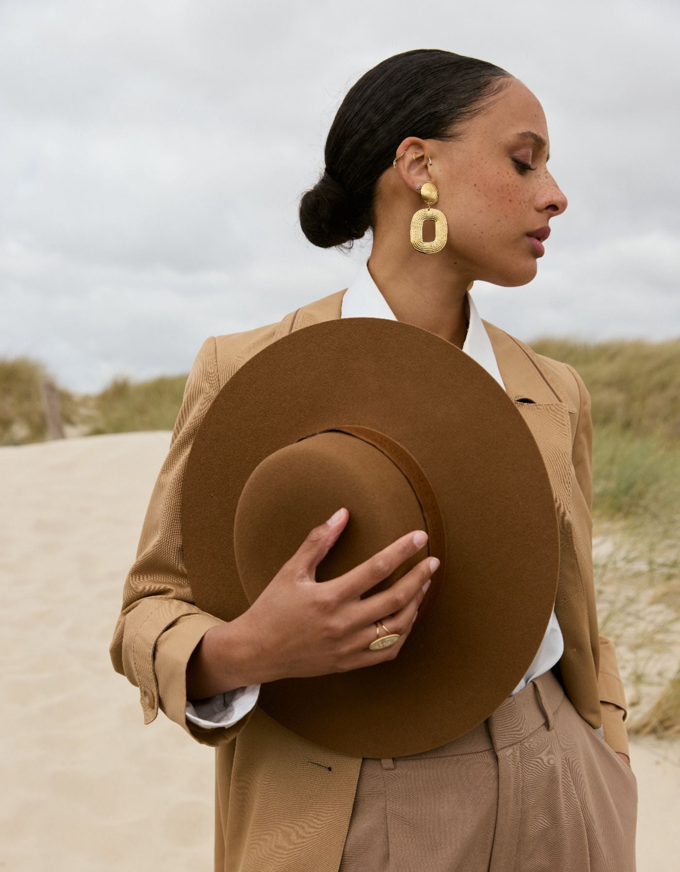 Une femme en manteau et chapeau en feutre brun sur la plage.
